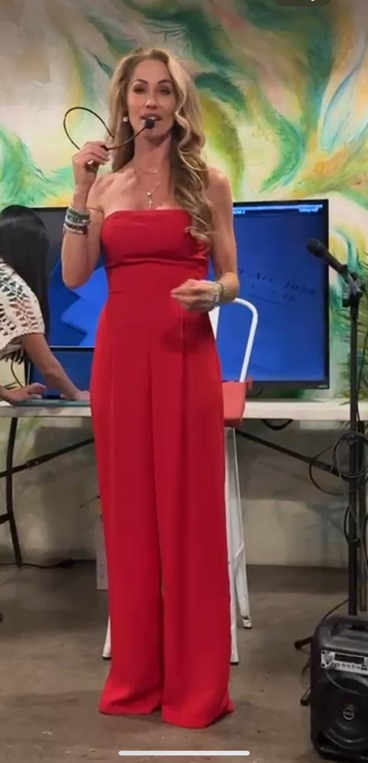 Melanie Marden in a red jumpsuit speaking with a headset microphone
