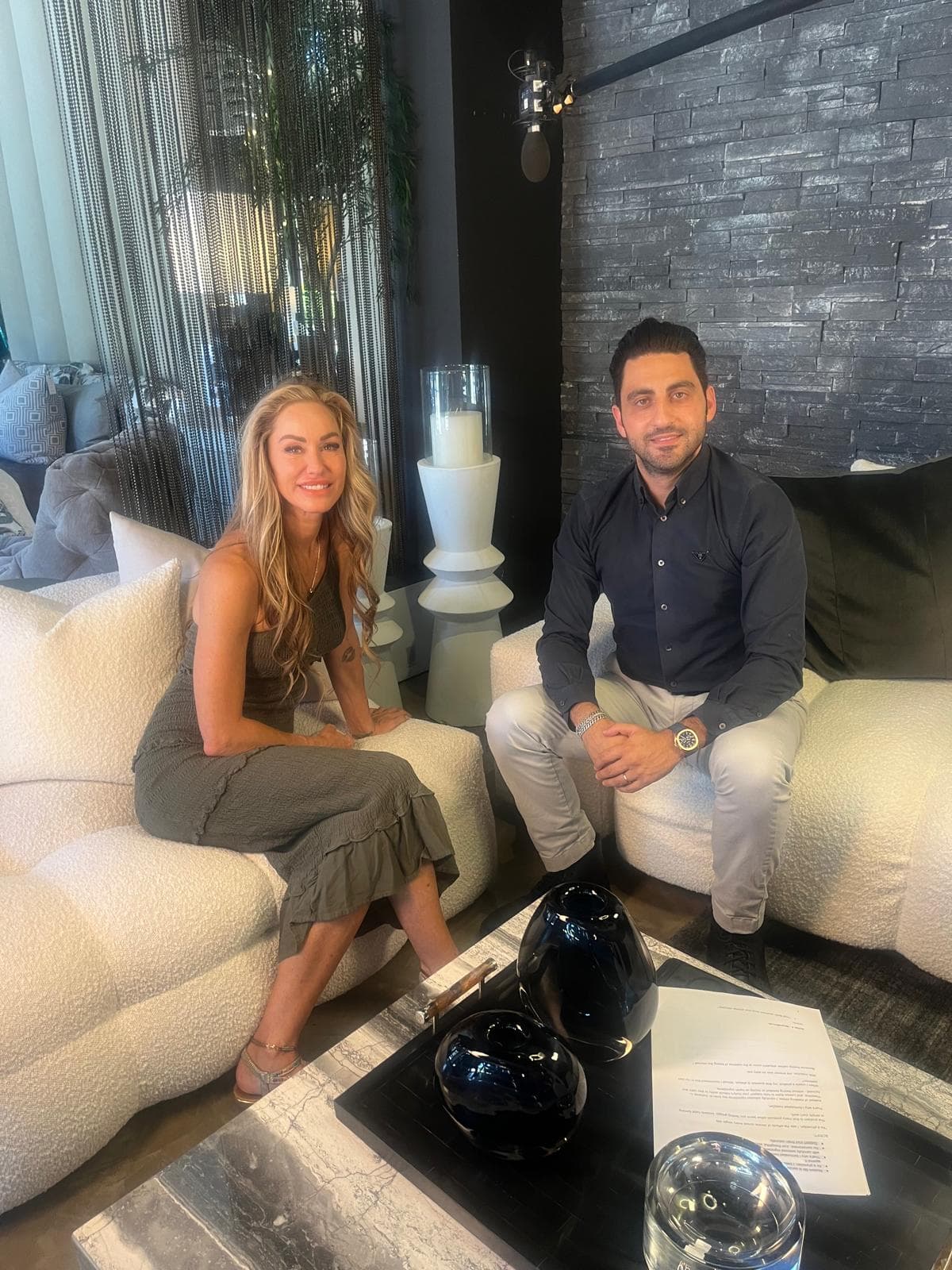 Melanie Marden seated on a white sofa across from a man in a dark shirt