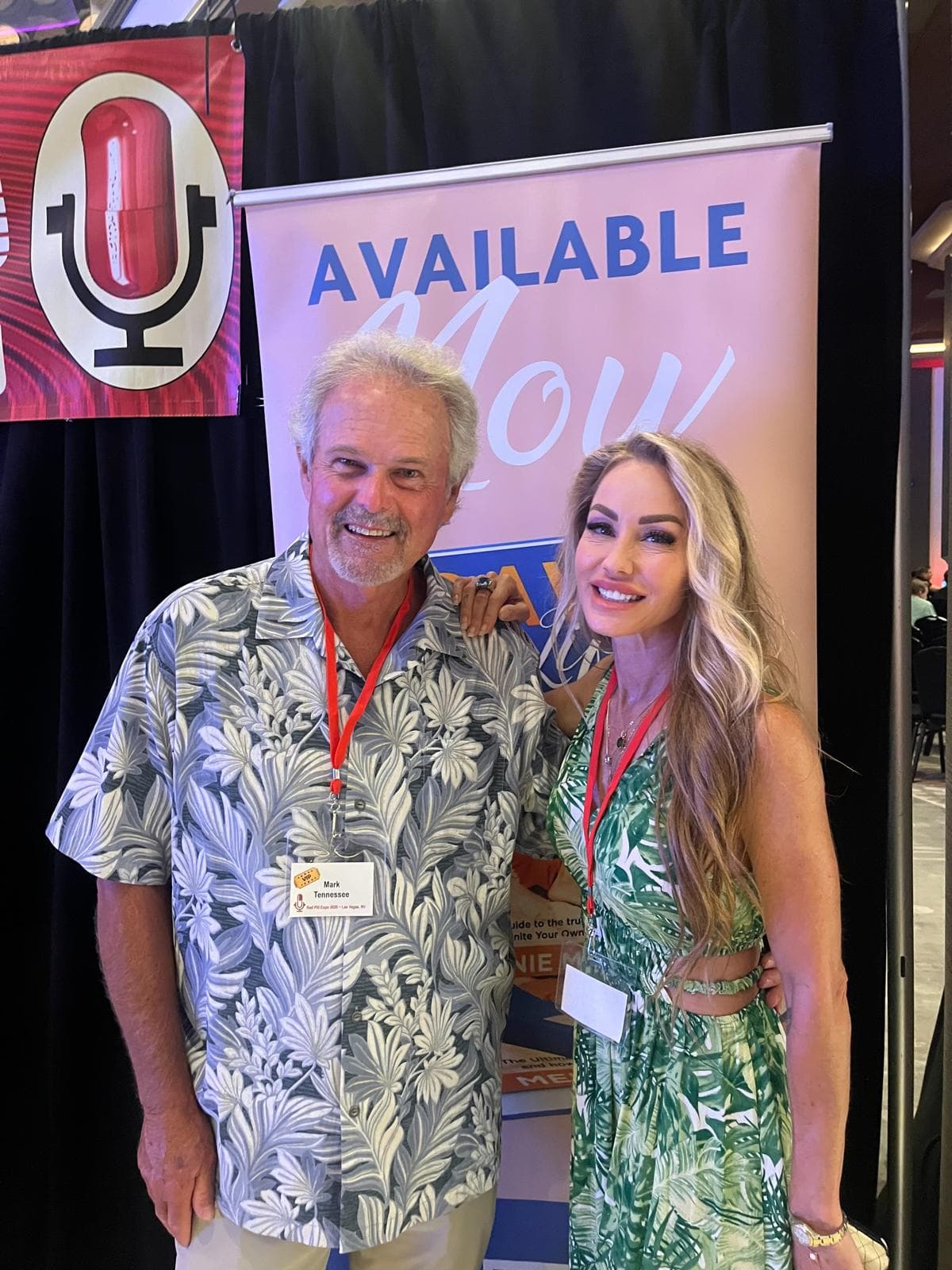 Melanie Marden with a guest in front of an Available Now banner for her book
